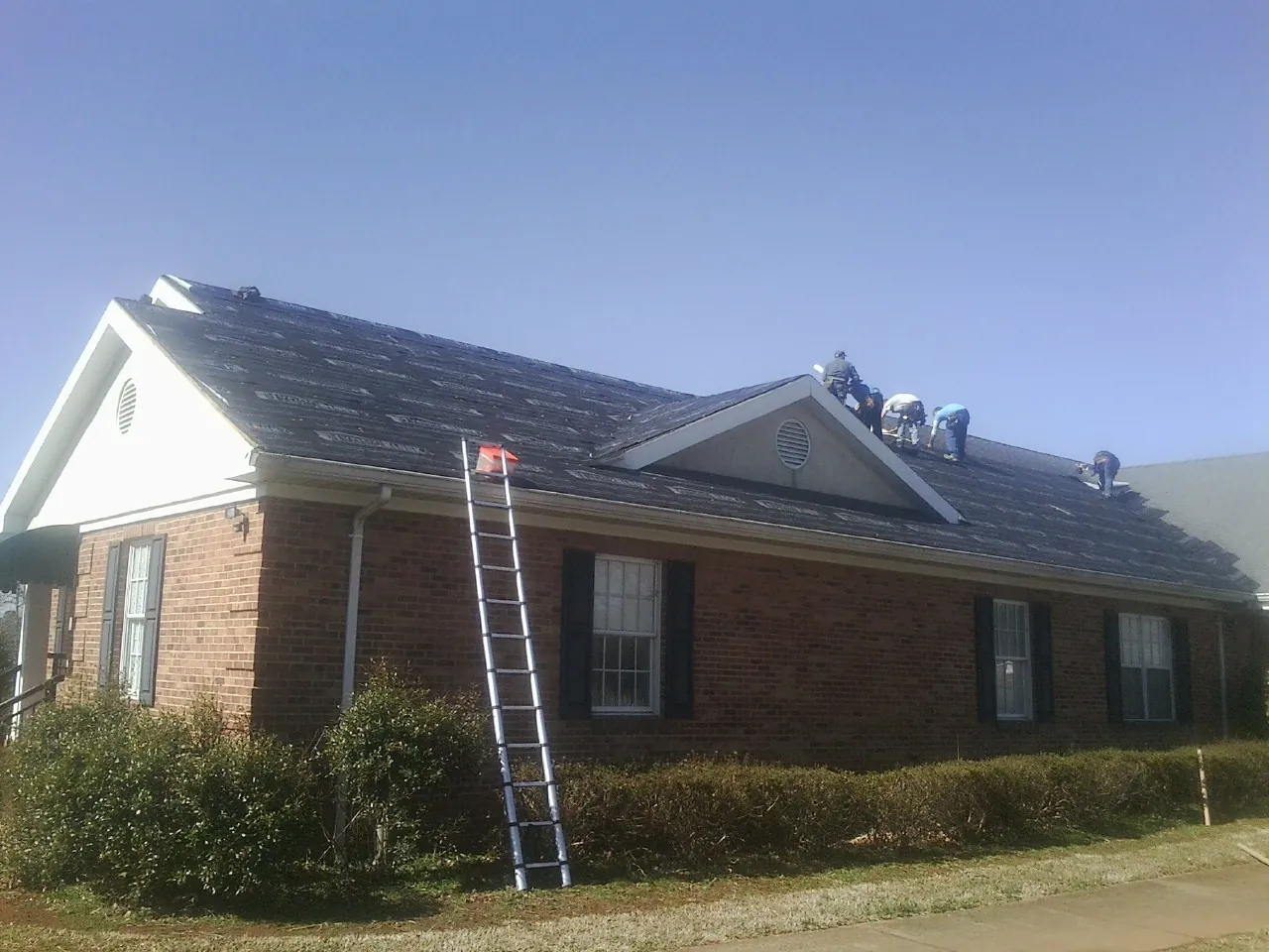 Crew tearing shingles off a brick ranch roof with a ladder set — Metal Roof Repair work by our crew in Sheridan