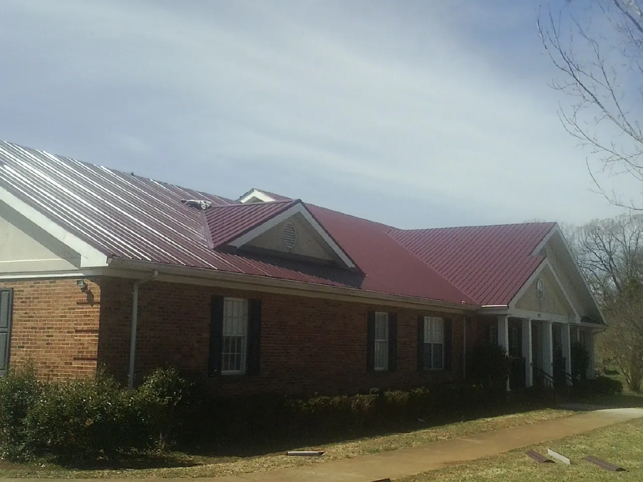 Red metal roof with gabled entries on a long brick building, from a Hail Damage Roof Repair job in Sheridan