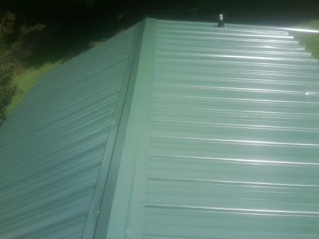 New green metal panels meeting at the ridge of a roof — Flat Roof Repair work by our crew in Sheridan