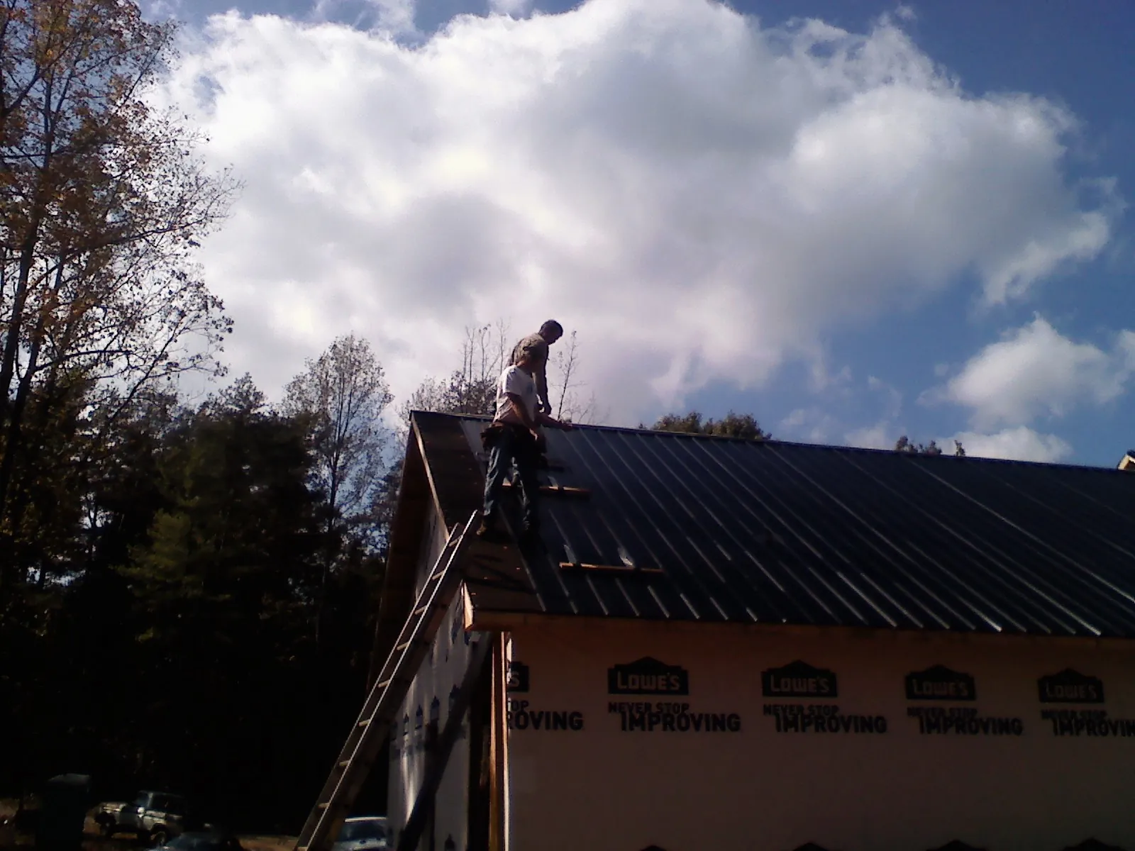Roofer fastening dark metal panels high against a cloudy sky, from a Roof Inspection job in Sheridan