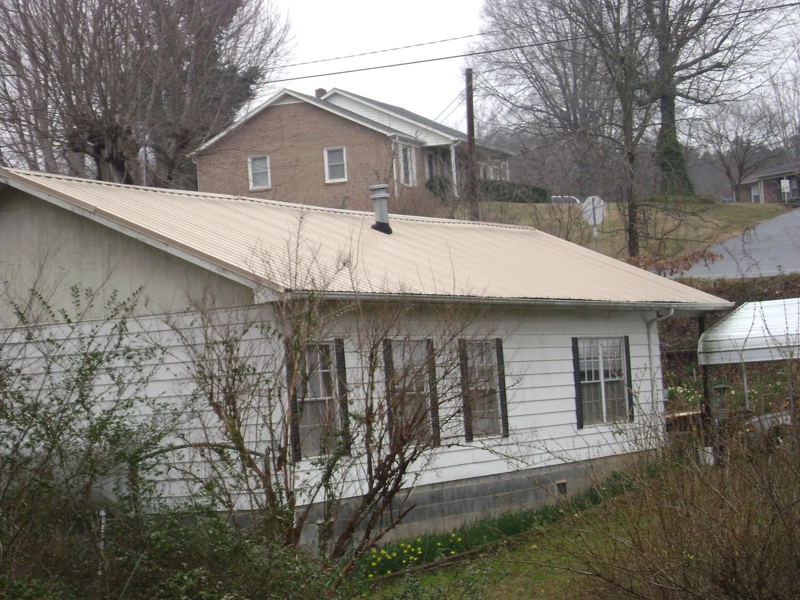 Tan metal roof on a white sided house set into a hillside — Commercial Roofing by Roofing Brothers in Sheridan
