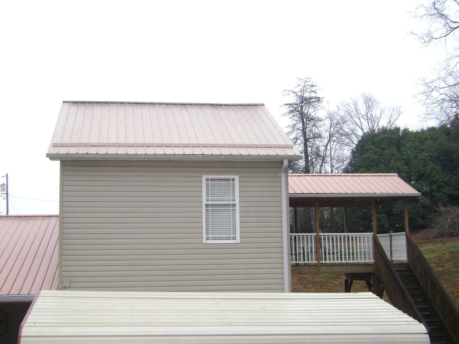 Tan metal roofs on a two story addition and attached porch, from a Roof Replacement job in Sheridan